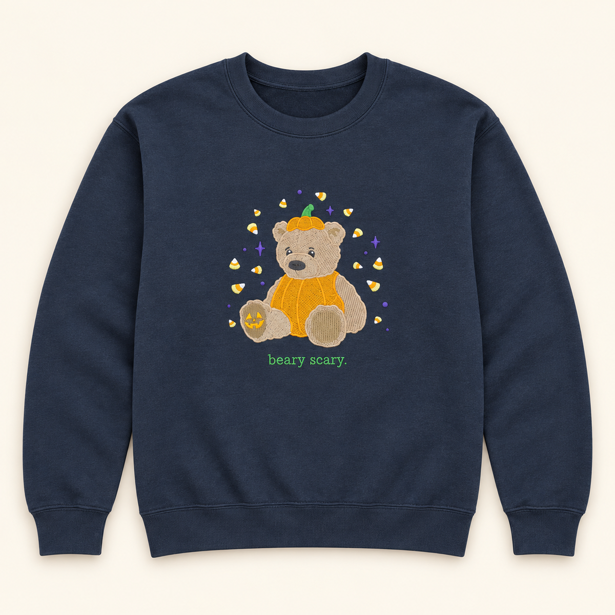 Dark navy Beary Scary embroidered sweatshirt with a teddy bear dressed as a pumpkin, candy corn, and purple stars on an ivory studio background