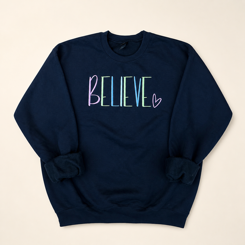 Navy BELIEVE embroidered sweatshirt on a warm ivory studio background
