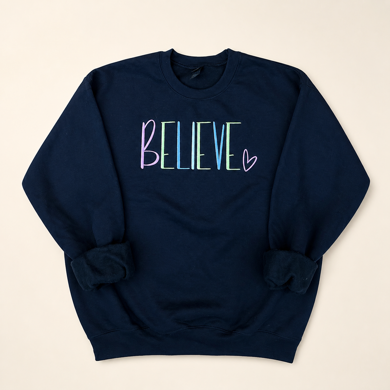 Navy BELIEVE embroidered sweatshirt on a warm ivory studio background