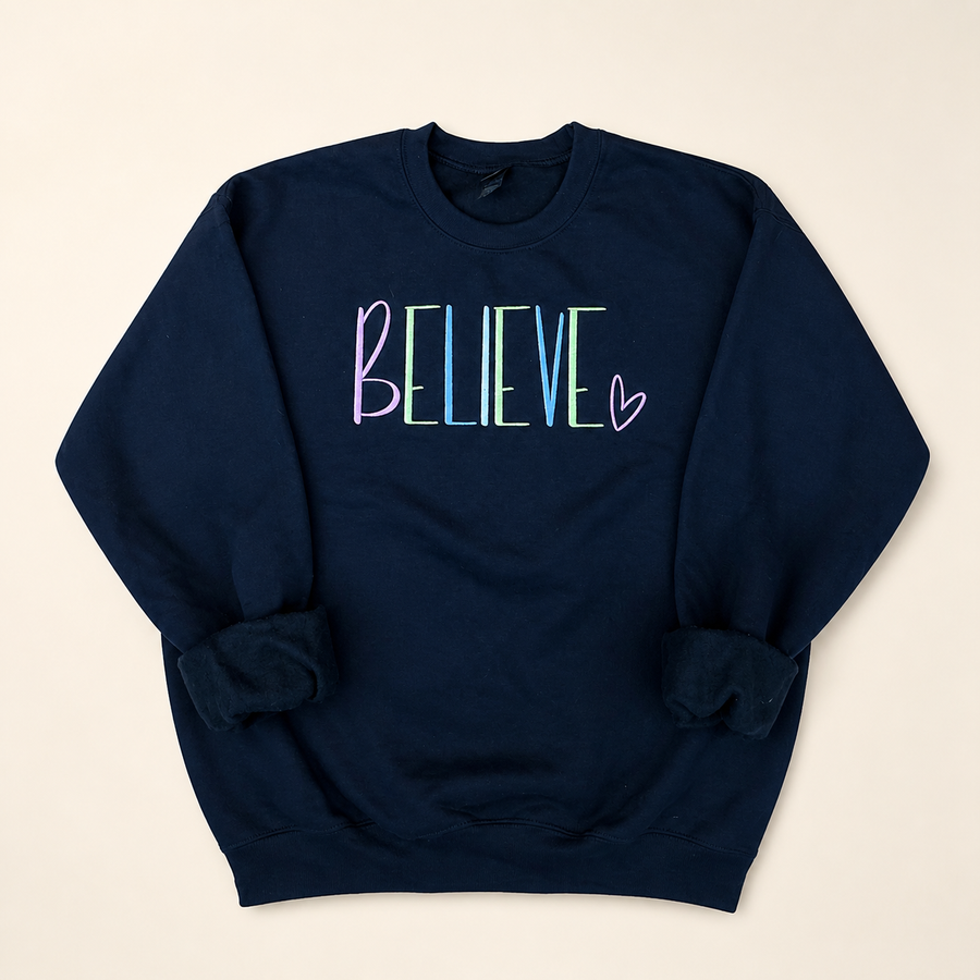 Navy BELIEVE embroidered sweatshirt on a warm ivory studio background