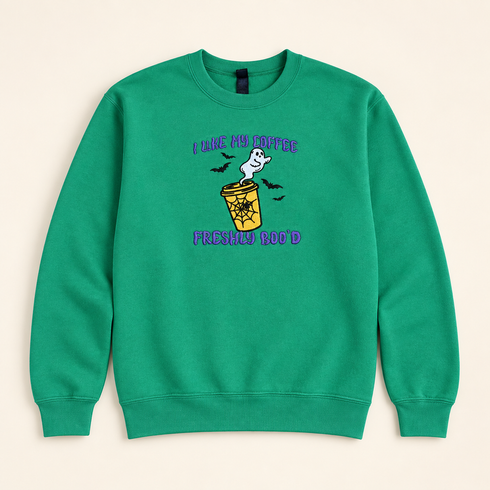 Green Freshly Boo’d Coffee embroidered sweatshirt, neatly arranged on a warm ivory studio background