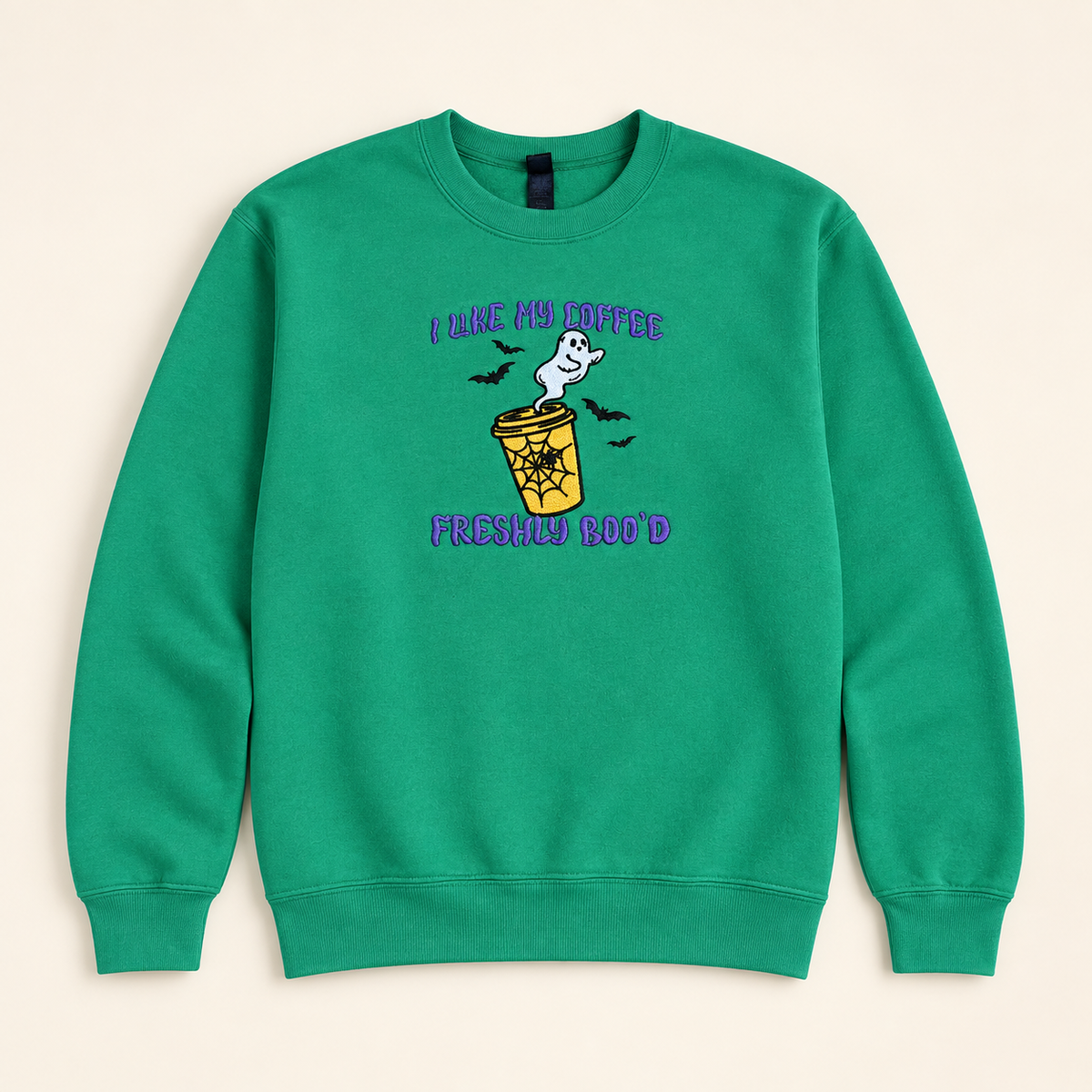 Green Freshly Boo’d Coffee embroidered sweatshirt, neatly arranged on a warm ivory studio background
