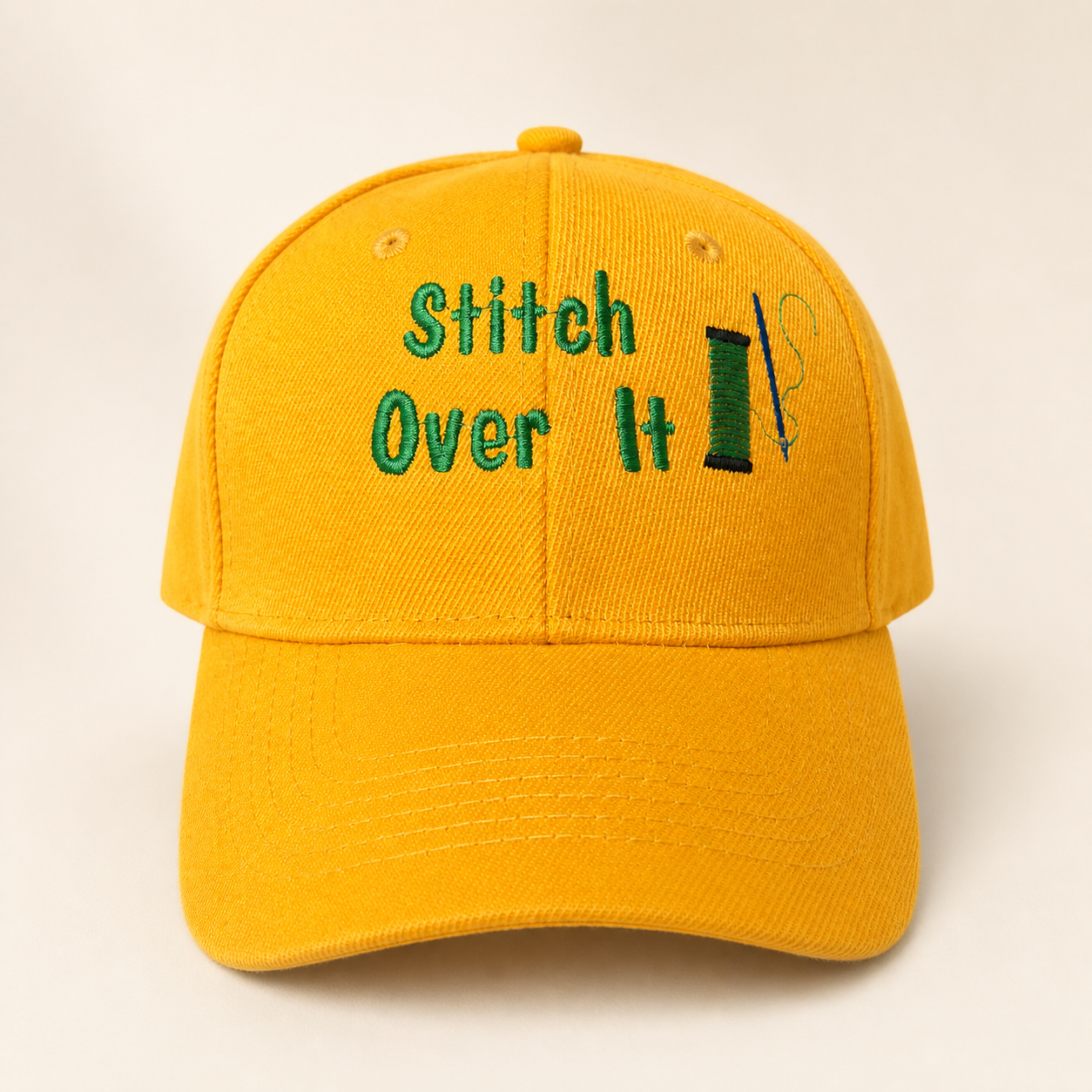 Yellow Stitch Over It logo hat on a warm ivory studio background